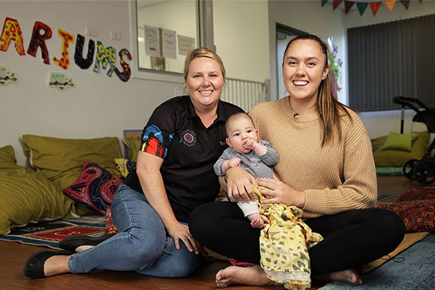 A young mum and her child smiling next a staff member from The Benevolent Society