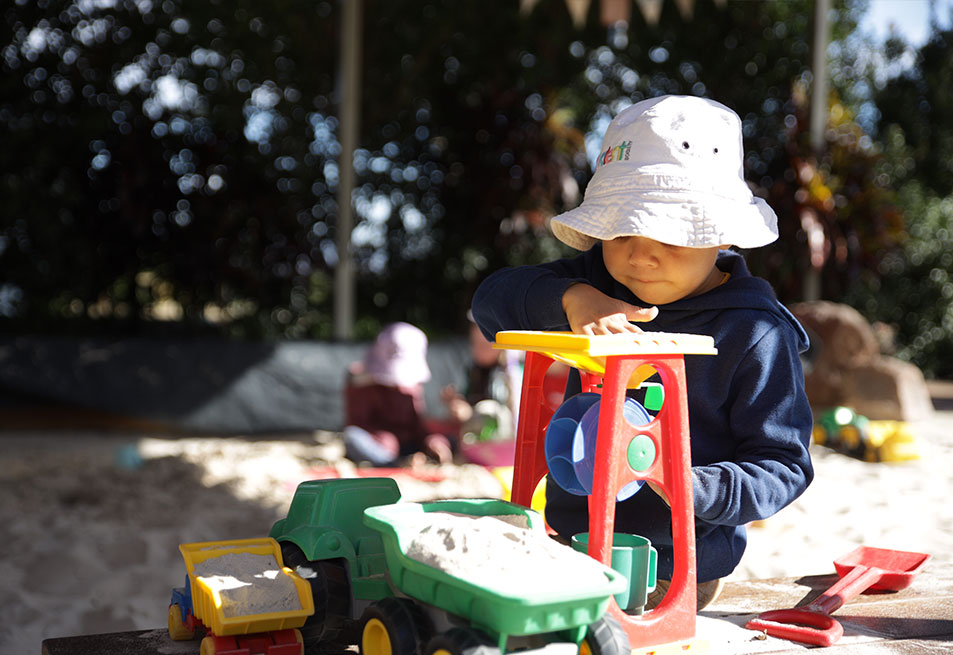 A young child playing with a toy truck. He is wearing a bucket hat with The Benevolent Society logo on it.