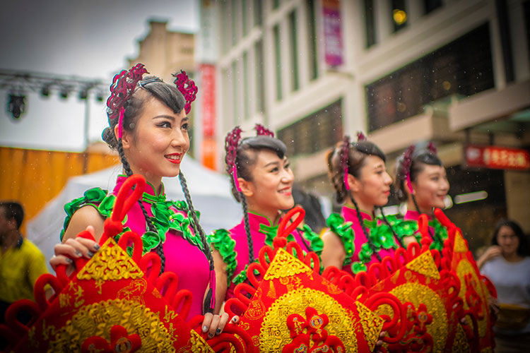 Women dressed in traditional Chinese garb for the Lunar Festival. They are smiling at passersbys.