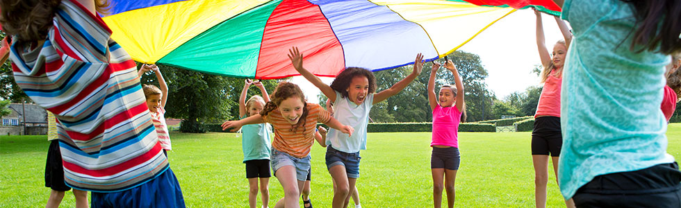 A group of young children playing underneath a multicoloured parachute