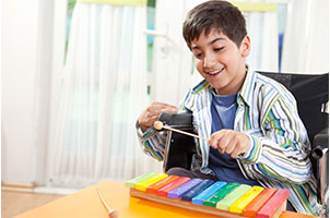 A young male wheelchair user having fun with a rainbow xylophone