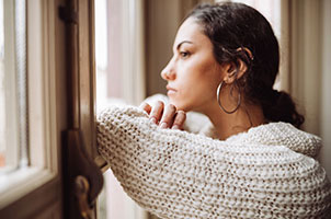 A woman in a cream coloured jumper looking solemnly out the window