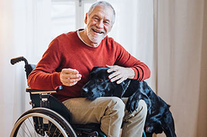 An older male wheelchair user wearing a red jumper with his black dog in his lap