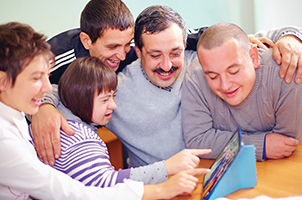 A photo of a group of people with disability smiling and interacting with a tablet