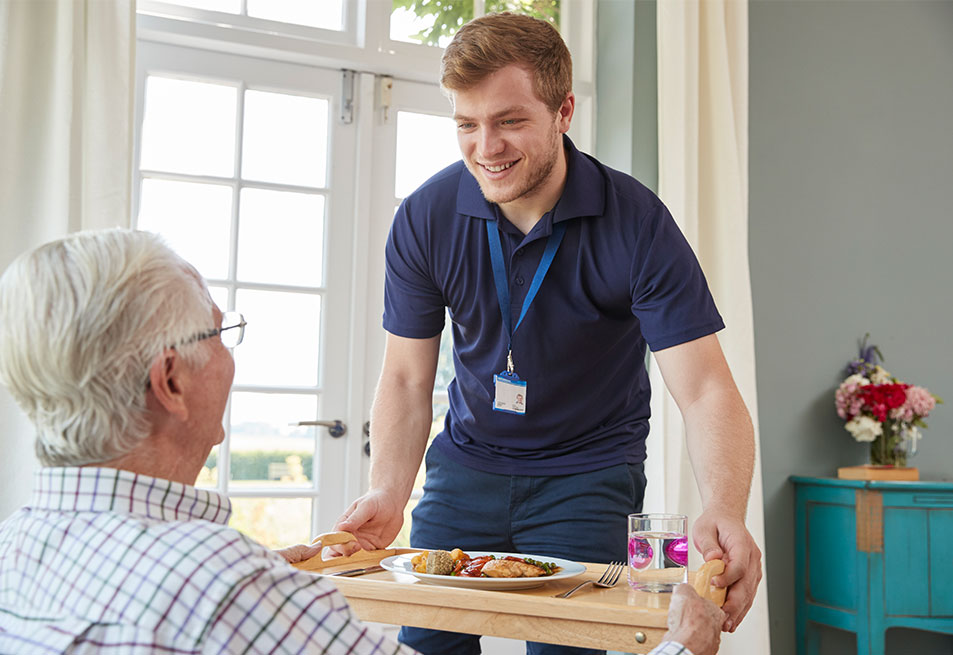 A male aged care worker placing a meal tray down to his client