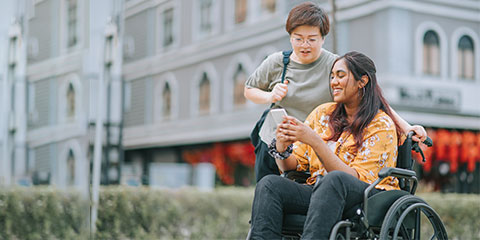 A wheelchair user with a friend outside looking at directions on a phone